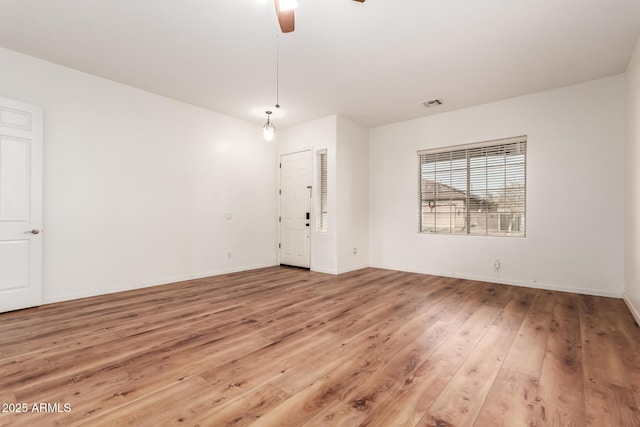 empty room featuring a ceiling fan, wood finished floors, visible vents, and baseboards