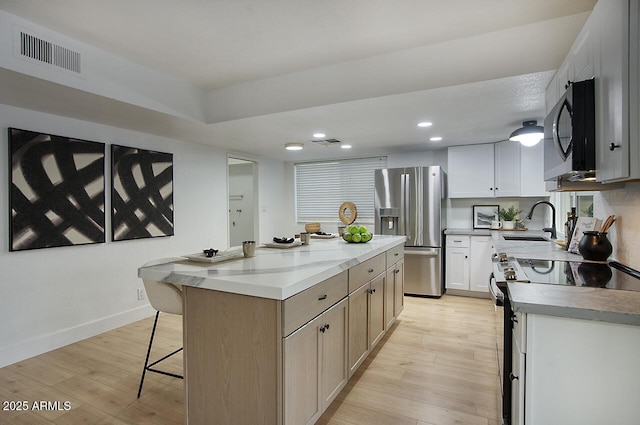 kitchen featuring light hardwood / wood-style floors, white cabinetry, appliances with stainless steel finishes, and a center island