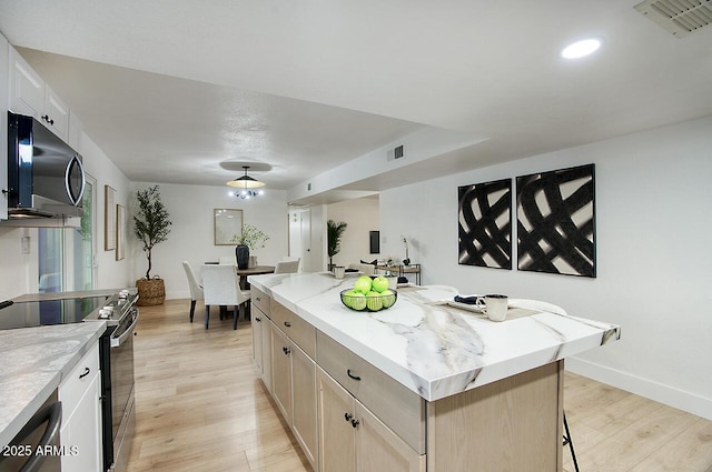 kitchen with light brown cabinetry, appliances with stainless steel finishes, a kitchen bar, light wood-type flooring, and a kitchen island