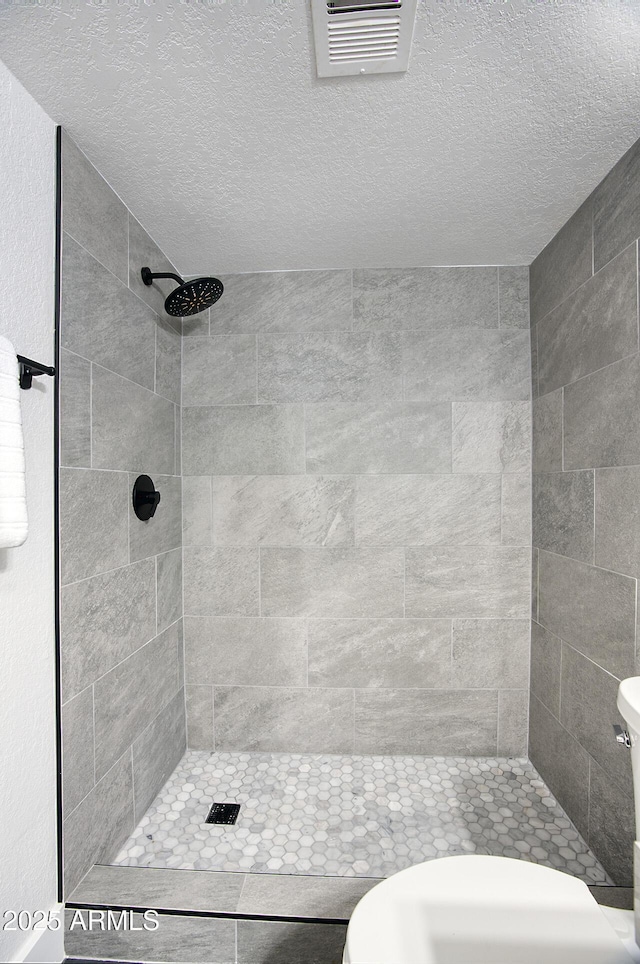 bathroom with a tile shower, toilet, and a textured ceiling