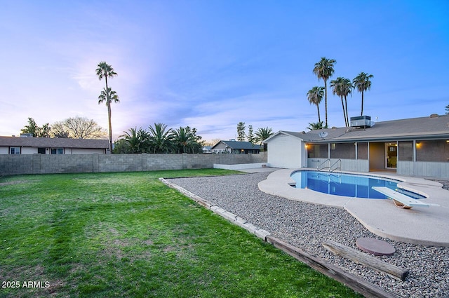 pool at dusk with a diving board, central AC unit, and a lawn