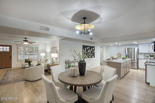 dining area with light hardwood / wood-style floors, a textured ceiling, and an inviting chandelier