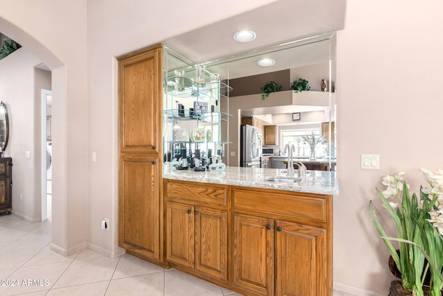 bar featuring sink, light stone counters, light tile patterned floors, and stainless steel refrigerator