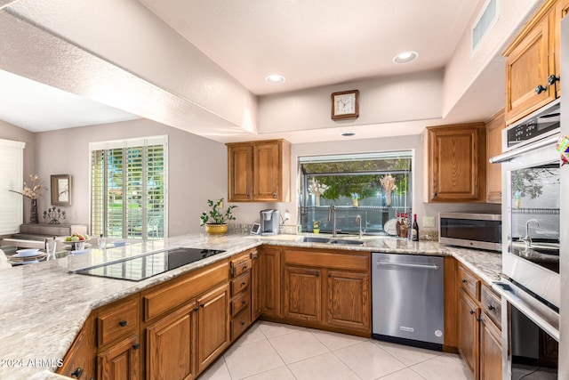 kitchen featuring light stone countertops, sink, kitchen peninsula, stainless steel appliances, and light tile patterned floors