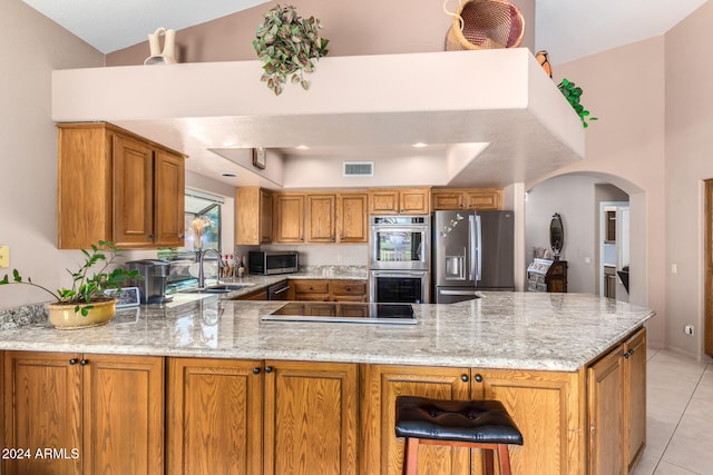 kitchen with kitchen peninsula, light tile patterned floors, light stone countertops, sink, and stainless steel appliances