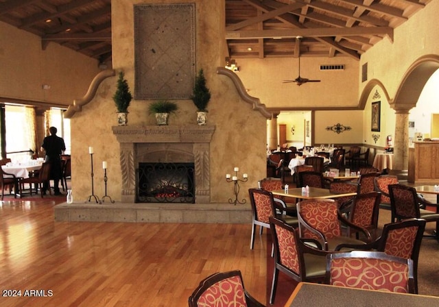 dining room featuring an outdoor fireplace, wood-type flooring, high vaulted ceiling, and ceiling fan