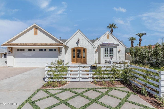 view of front of home with an attached garage, stucco siding, concrete driveway, a fenced front yard, and brick siding