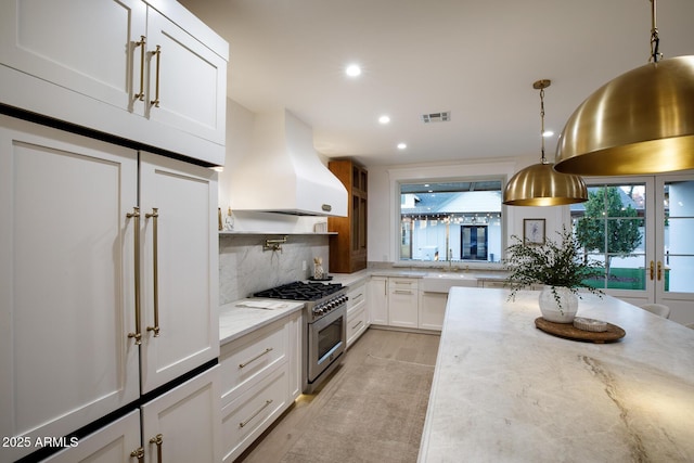 kitchen with visible vents, island exhaust hood, white cabinetry, stainless steel stove, and decorative backsplash