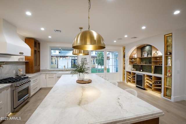 kitchen with high end range, light stone counters, visible vents, wine cooler, and exhaust hood