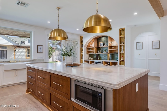 kitchen with visible vents, a sink, stainless steel microwave, white cabinetry, and light wood-style floors