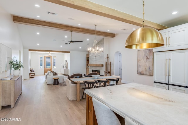 dining area with visible vents, vaulted ceiling with beams, a fireplace, arched walkways, and light wood-style floors