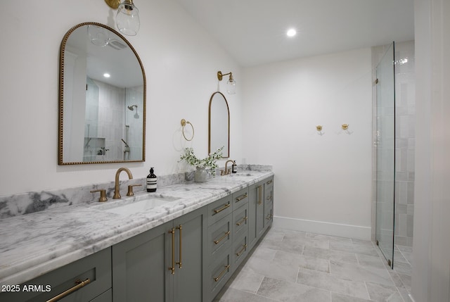 bathroom with double vanity, tiled shower, baseboards, and a sink