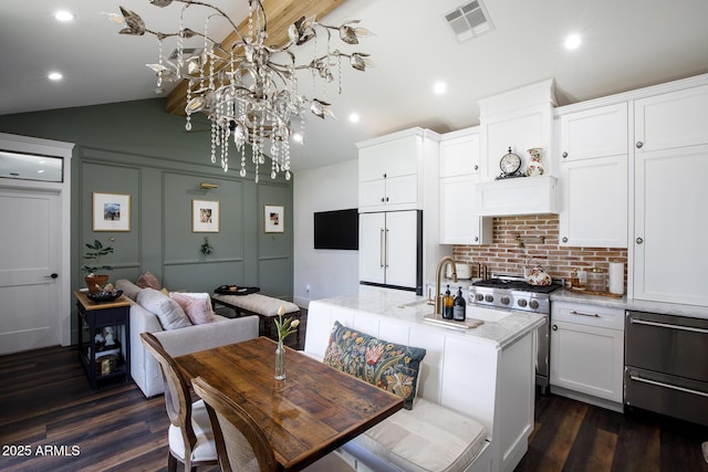 kitchen with paneled fridge, visible vents, a sink, white cabinets, and vaulted ceiling