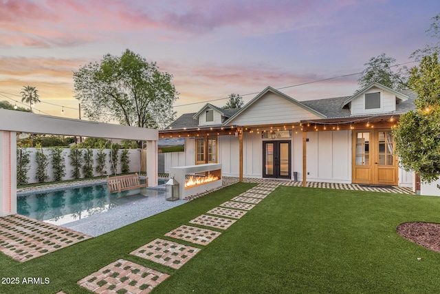 back of house featuring board and batten siding, a fire pit, a lawn, french doors, and a fenced backyard