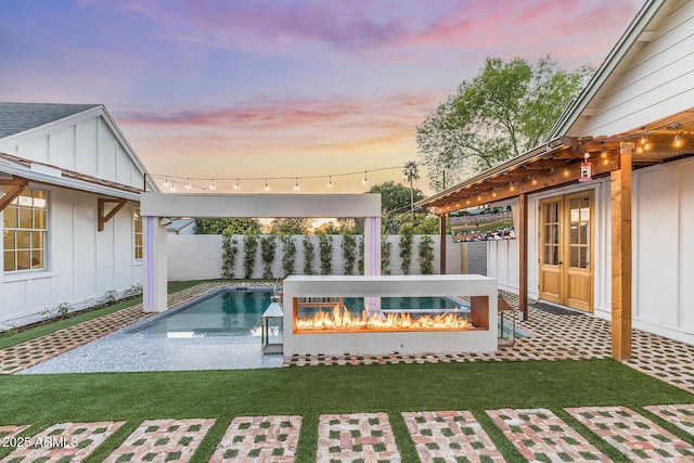 pool at dusk featuring a pool, a lawn, french doors, and a fenced backyard