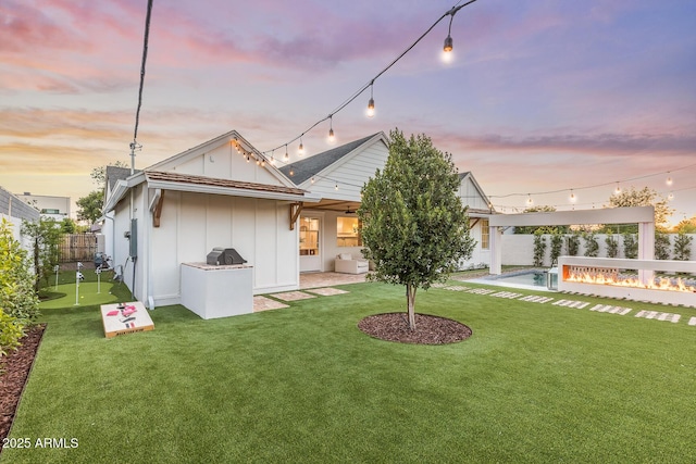 back of house with board and batten siding, a fire pit, a fenced backyard, a yard, and a patio area