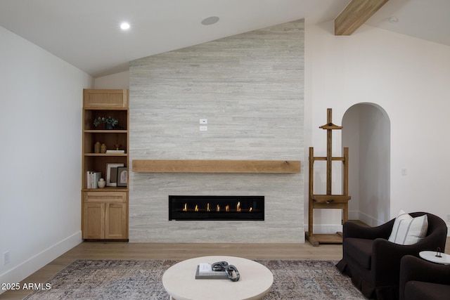 living area with lofted ceiling with beams, baseboards, a large fireplace, and wood finished floors