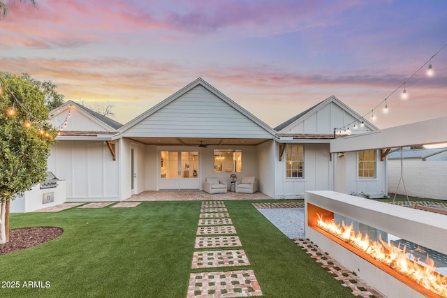 back of house at dusk with a patio area, a lawn, board and batten siding, and french doors