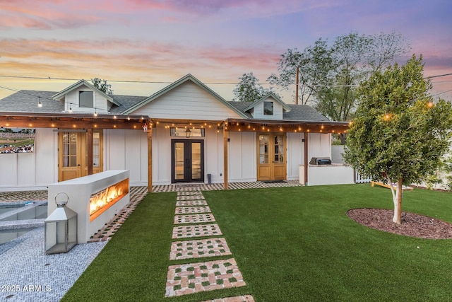 rear view of property featuring french doors, a yard, board and batten siding, and roof with shingles