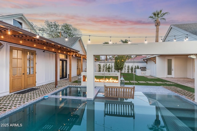 pool at dusk with fence, a fire pit, and a patio area