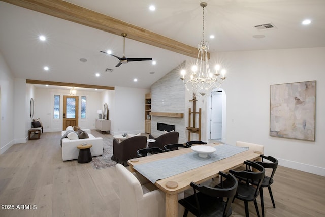 dining area featuring visible vents, beamed ceiling, arched walkways, a stone fireplace, and light wood finished floors