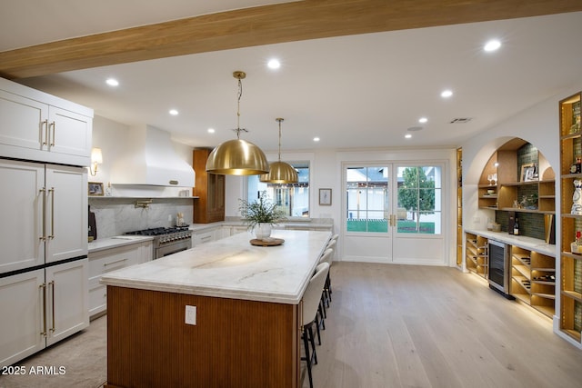 kitchen with backsplash, white cabinets, wall chimney range hood, and light stone countertops