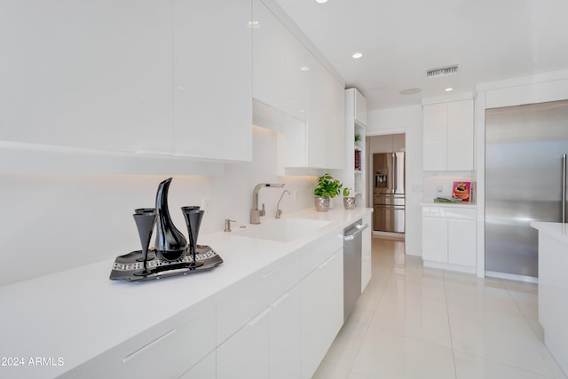 kitchen with appliances with stainless steel finishes, sink, light tile patterned floors, and white cabinets