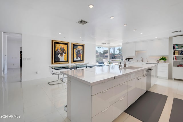 kitchen featuring white cabinets, light tile patterned flooring, a large island with sink, and sink