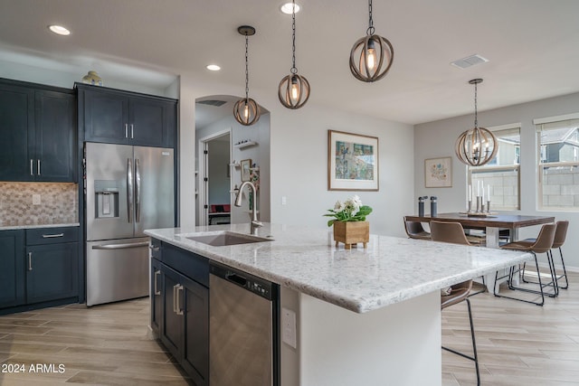 kitchen featuring decorative backsplash, appliances with stainless steel finishes, light hardwood / wood-style floors, an island with sink, and sink