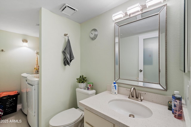 bathroom featuring washing machine and clothes dryer, vanity, and toilet