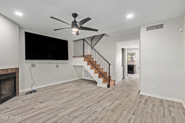 5704 E Aire Libre Ave Unit 1093, Scottsdale, AZ 85254 - unfurnished living room with a tiled fireplace, a ceiling fan, a textured ceiling, wood finished floors, and stairway