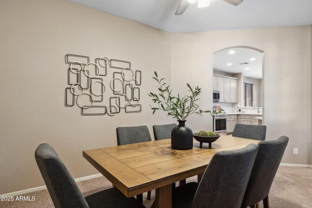 dining room featuring baseboards, arched walkways, light carpet, and ceiling fan