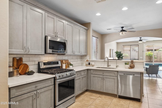 kitchen with gray cabinets, a sink, stainless steel appliances, a peninsula, and decorative backsplash