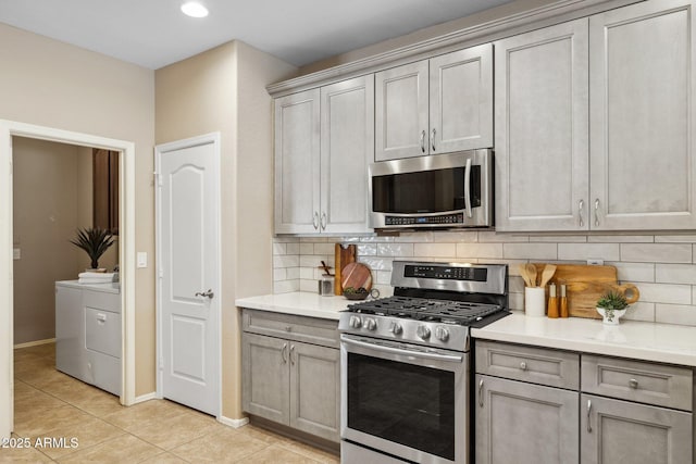 kitchen with light tile patterned floors, appliances with stainless steel finishes, gray cabinets, and washing machine and clothes dryer