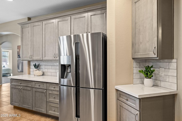 kitchen featuring tasteful backsplash, arched walkways, stainless steel fridge, and gray cabinetry