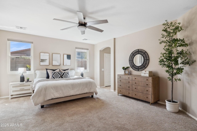 carpeted bedroom with visible vents, arched walkways, baseboards, and a ceiling fan