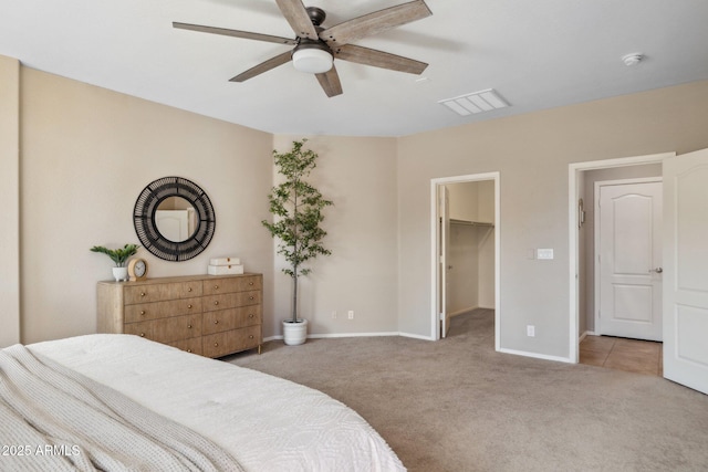 carpeted bedroom with visible vents, baseboards, a walk in closet, and a ceiling fan