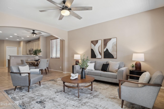 living area with a ceiling fan, recessed lighting, arched walkways, light tile patterned floors, and baseboards