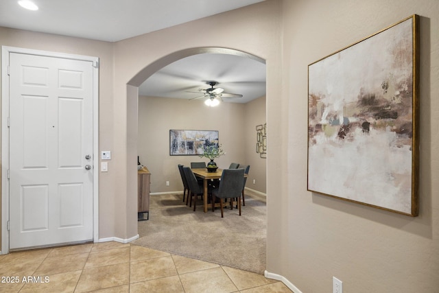 foyer featuring baseboards, ceiling fan, light colored carpet, light tile patterned floors, and arched walkways