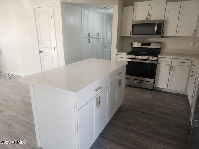 kitchen with appliances with stainless steel finishes, dark wood-type flooring, white cabinetry, and a center island