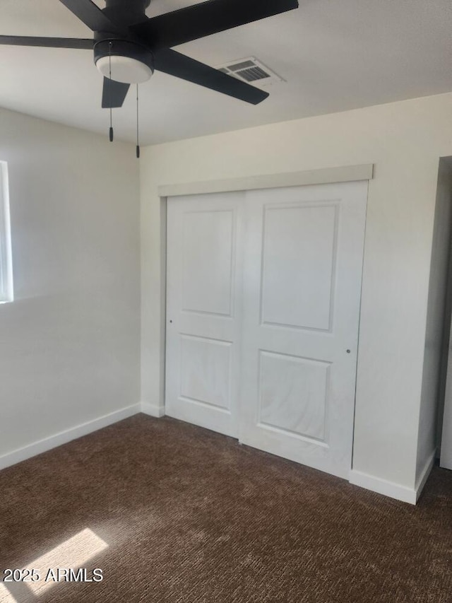 unfurnished bedroom with dark carpet, baseboards, a closet, and a ceiling fan