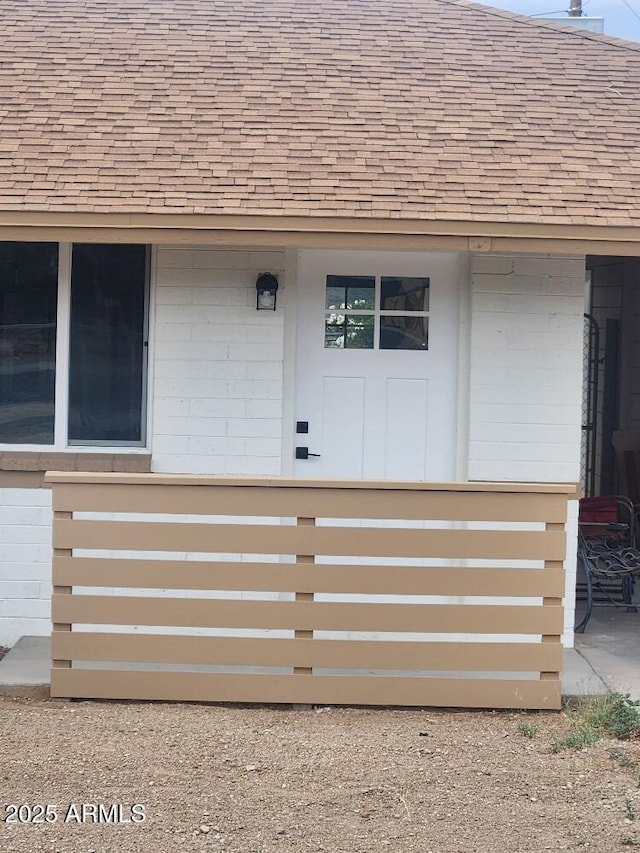 view of exterior entry with roof with shingles