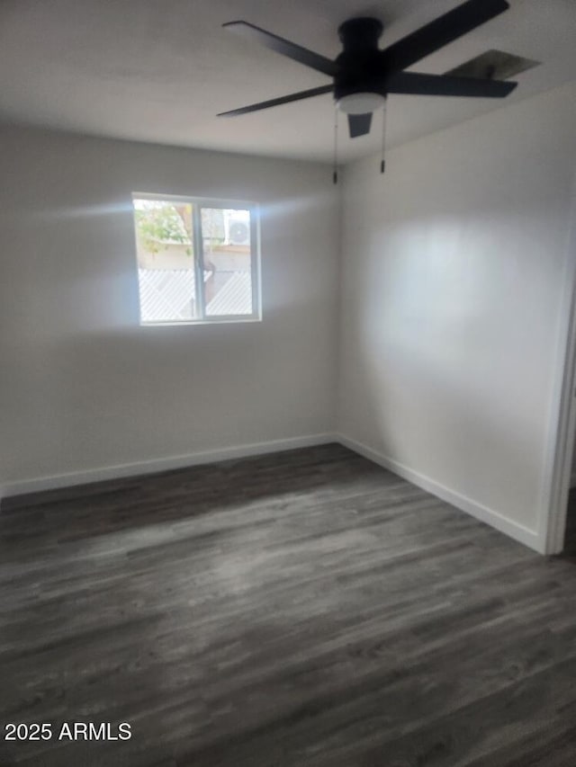 spare room featuring baseboards, dark wood-type flooring, and a ceiling fan