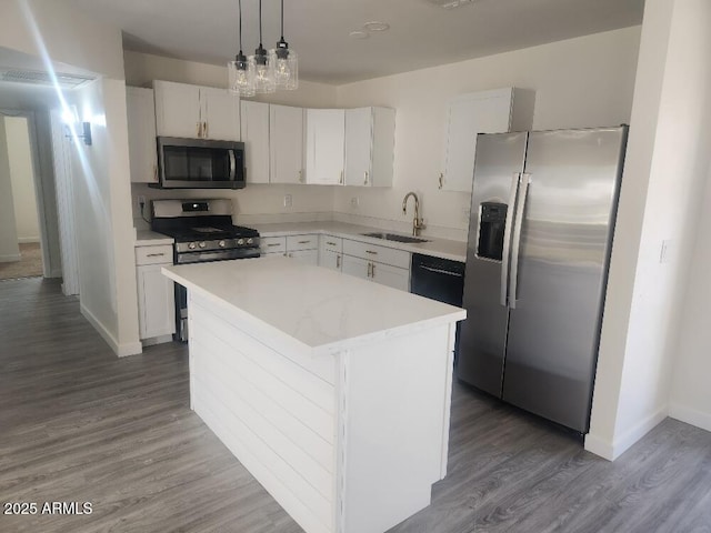 kitchen featuring appliances with stainless steel finishes, a sink, a kitchen island, wood finished floors, and light countertops