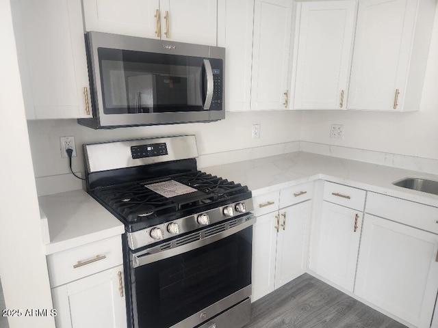 kitchen featuring stainless steel appliances, white cabinetry, wood finished floors, and light stone countertops