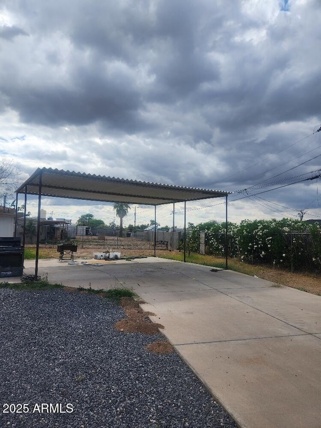 view of parking / parking lot featuring fence, a detached carport, and concrete driveway