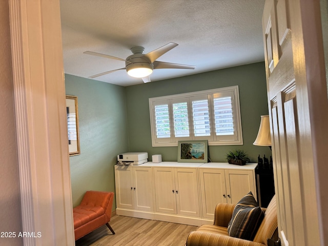 living area with a textured ceiling, ceiling fan, and light wood-type flooring