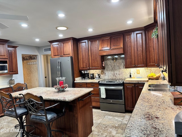 kitchen with a kitchen island, stainless steel appliances, light stone countertops, a kitchen bar, and decorative backsplash