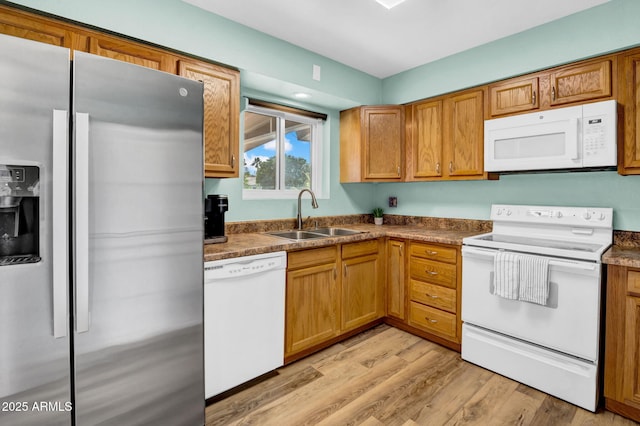 kitchen with white appliances, brown cabinetry, a sink, and light wood-style flooring