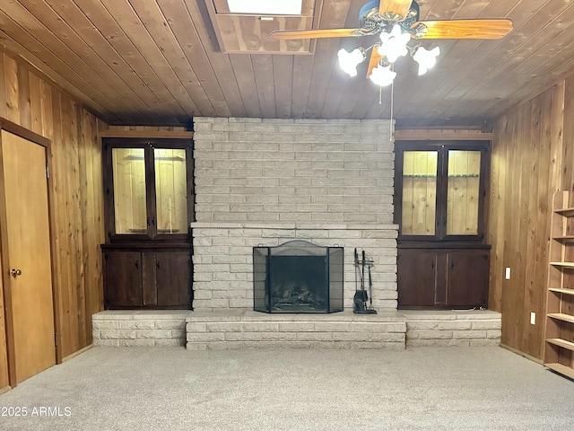 unfurnished living room with ceiling fan, a brick fireplace, wooden walls, carpet, and wood ceiling